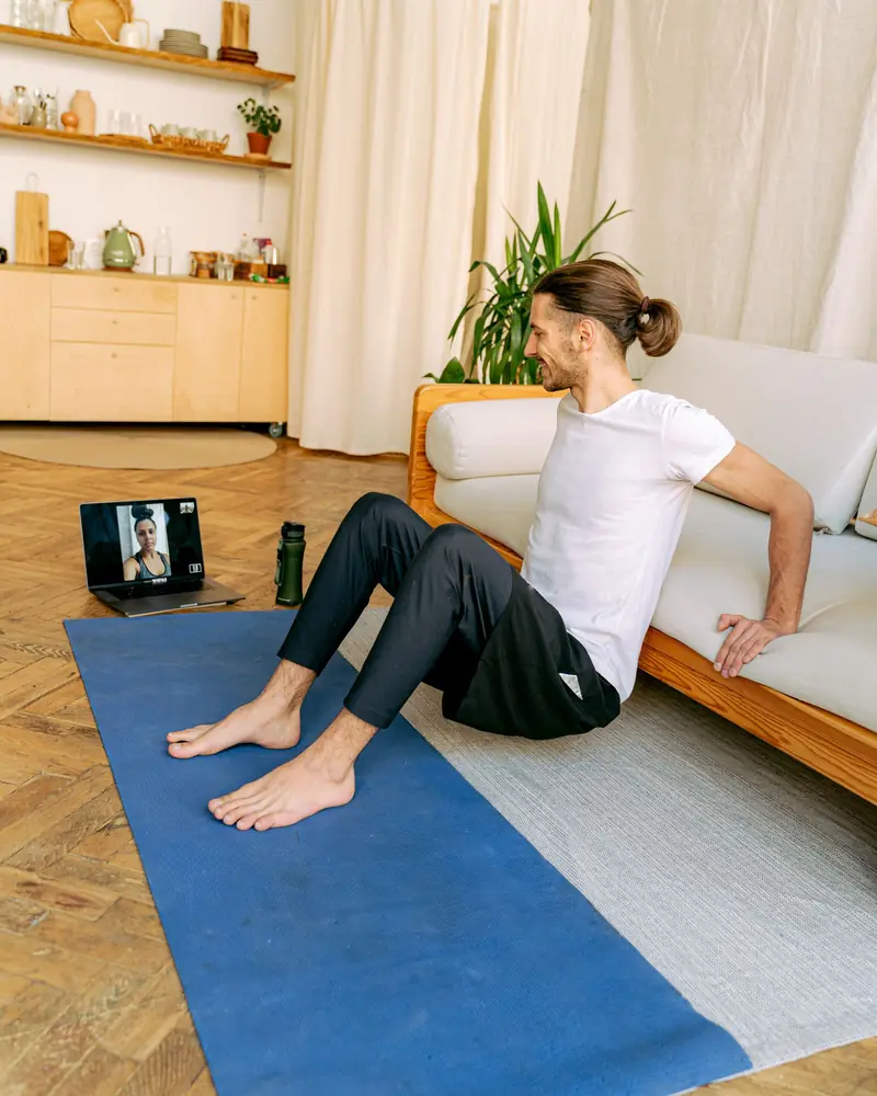A man doing a guided exercise at home, his physiotherapist on the laptop in front of him.