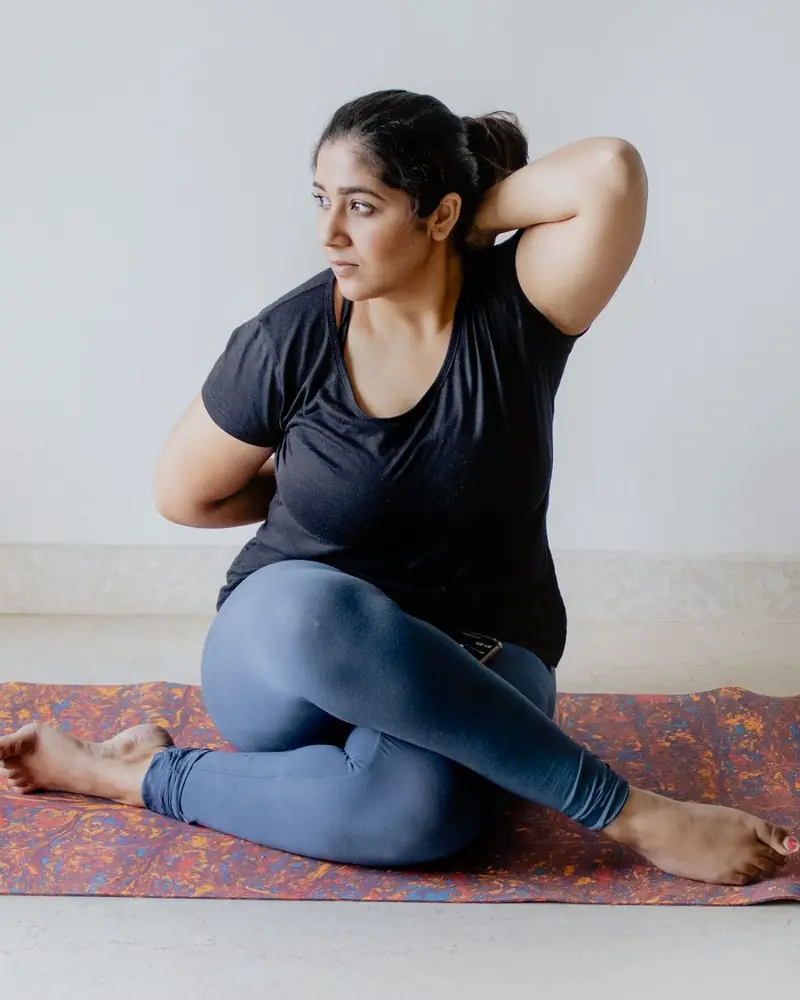A woman taking an unhurried seated stretch on a mat at home.